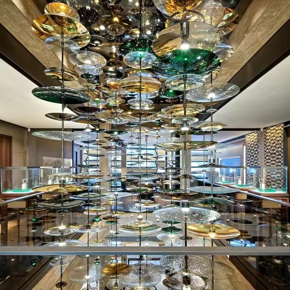 This is an artistic multi-layer glass disc chandelier, composed of multi-colored glass discs (gold, green, transparent, etc.) hung in multiple layers, featuring a strong artistic sense and visual hierarchy. It is used for space lighting and artistic decoration, creating a luxurious artistic atmosphere. It is suitable for high-end commercial exhibition halls, art spaces, luxury hotel lobbies and other places.