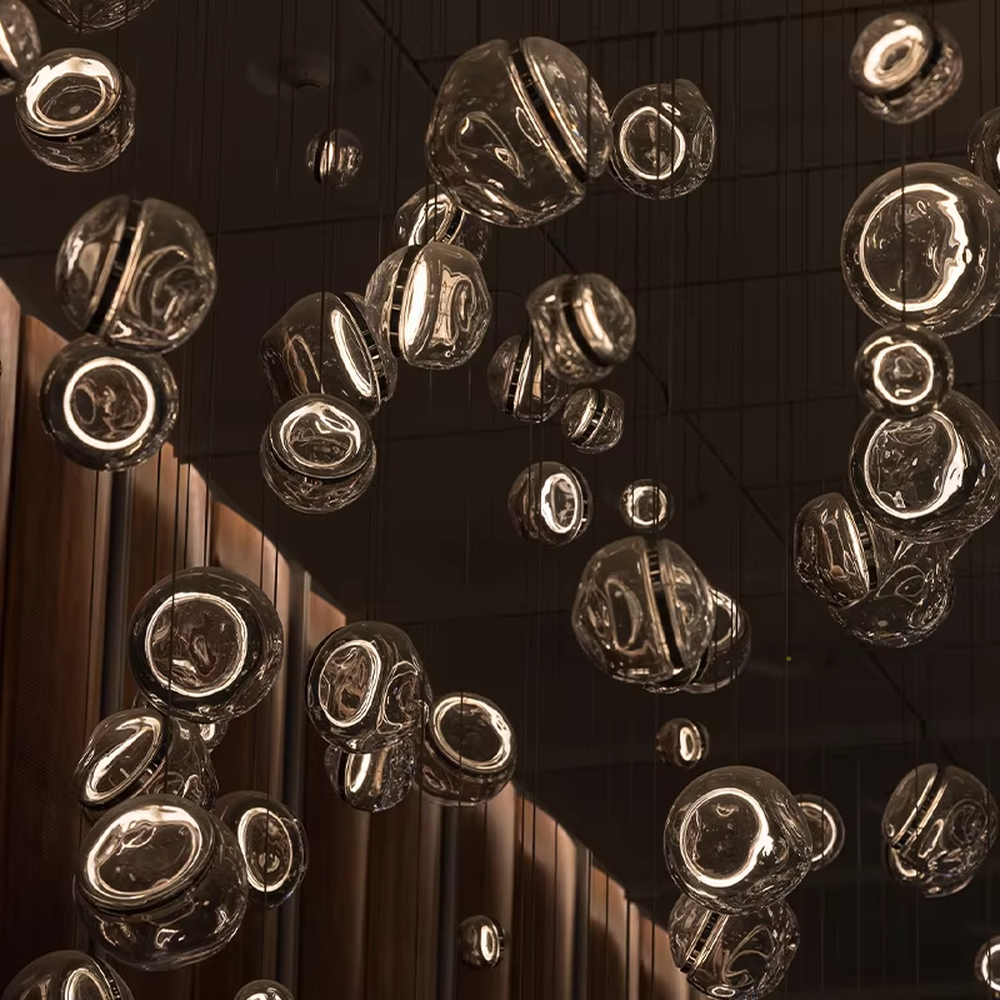 This is an artistic installation-style transparent glass ball chandelier, with numerous transparent glass balls of different sizes and shapes hanging in a scattered manner by thin wires. It features soft lighting and a strong sense of modern art and visual hierarchy. It is used for space lighting and artistic decoration, creating a modern artistic and ethereal atmosphere. Suitable for high-end hotel lobbies, art exhibition halls, atriums of large commercial centers and other places.
