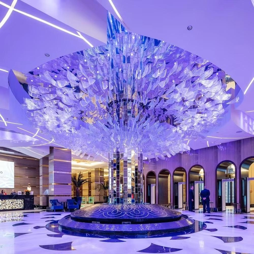 This is a large artistic crystal chandelier, composed of numerous irregular transparent sheet-like components. It has a layered, art-sculpture-like design and presents a luxurious and dreamy effect with purple lighting. It is used for decorating the space and providing lighting, with both artistic sense and practicality. It is suitable for high-end hotel lobbies, luxury casinos, large banquet halls and other high-end places.