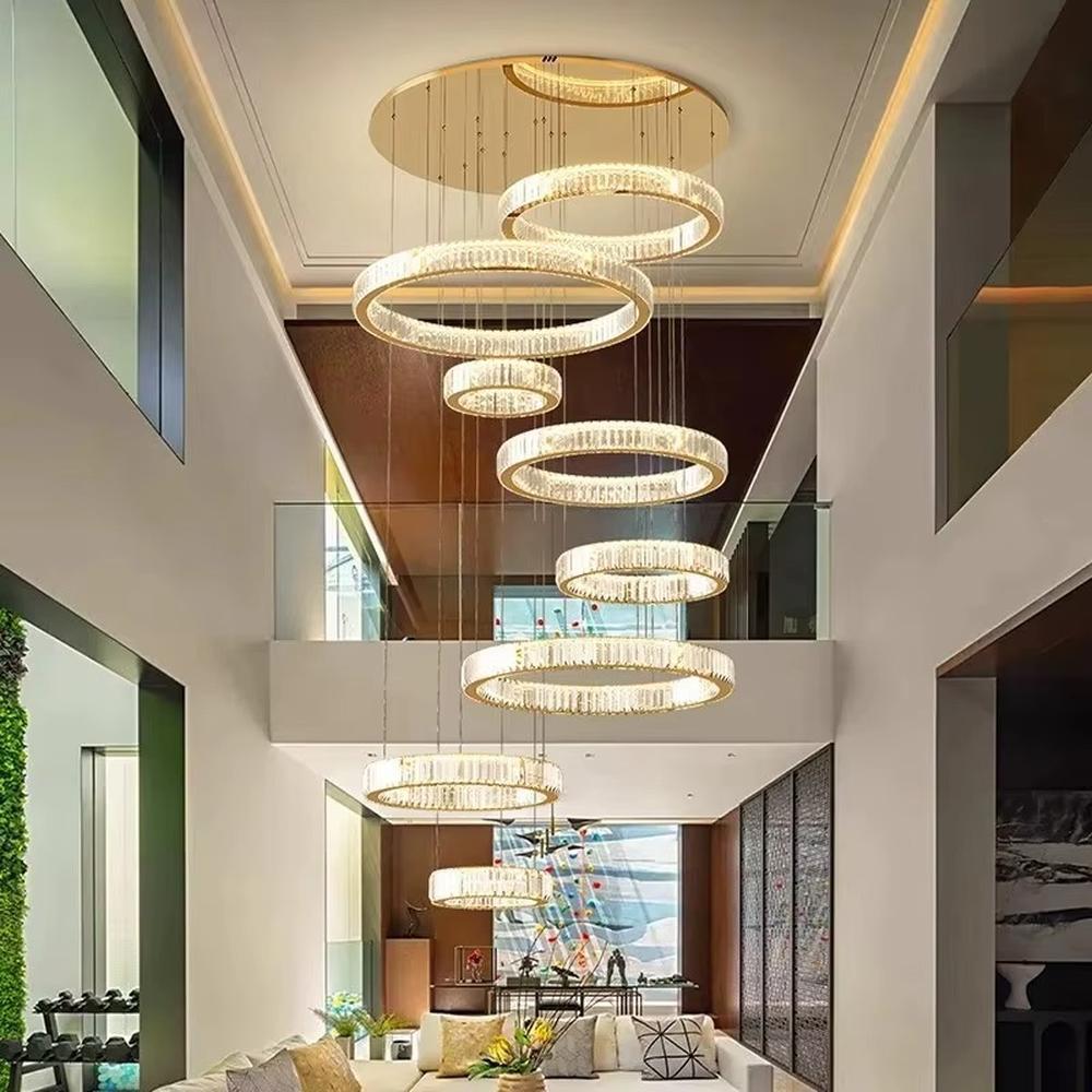 This is a luxury multi-layer circular crystal chandelier, with a golden base and staggered hanging crystal ring lamp bodies. It features a luxurious and grand design, shining brightly under light. It is used for space lighting and decoration, creating a high-end and luxurious ambiance. It is suitable for double-height living rooms in villas, lobbies of high-end hotels, luxury clubs and other places.