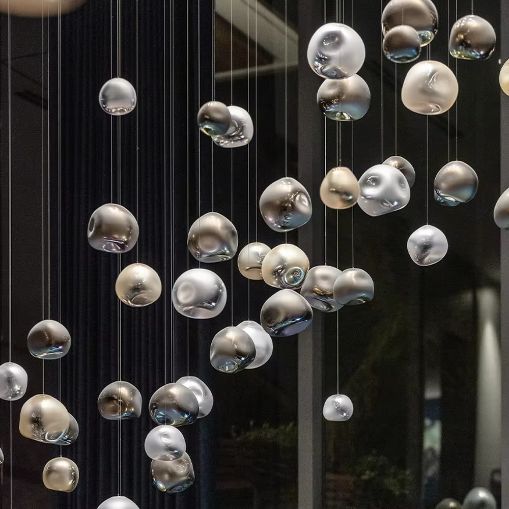 This is an artistic installation-style metal-textured glass sphere chandelier, with multiple irregular glass sphere lamps hanging in a scattered manner, featuring strong artistic sense, and the light reflects a unique visual effect. It is used for space lighting and artistic decoration, creating an artistic and modern atmosphere. Suitable for high-end hotel lobbies, art exhibition halls, modern art home living rooms and other places.