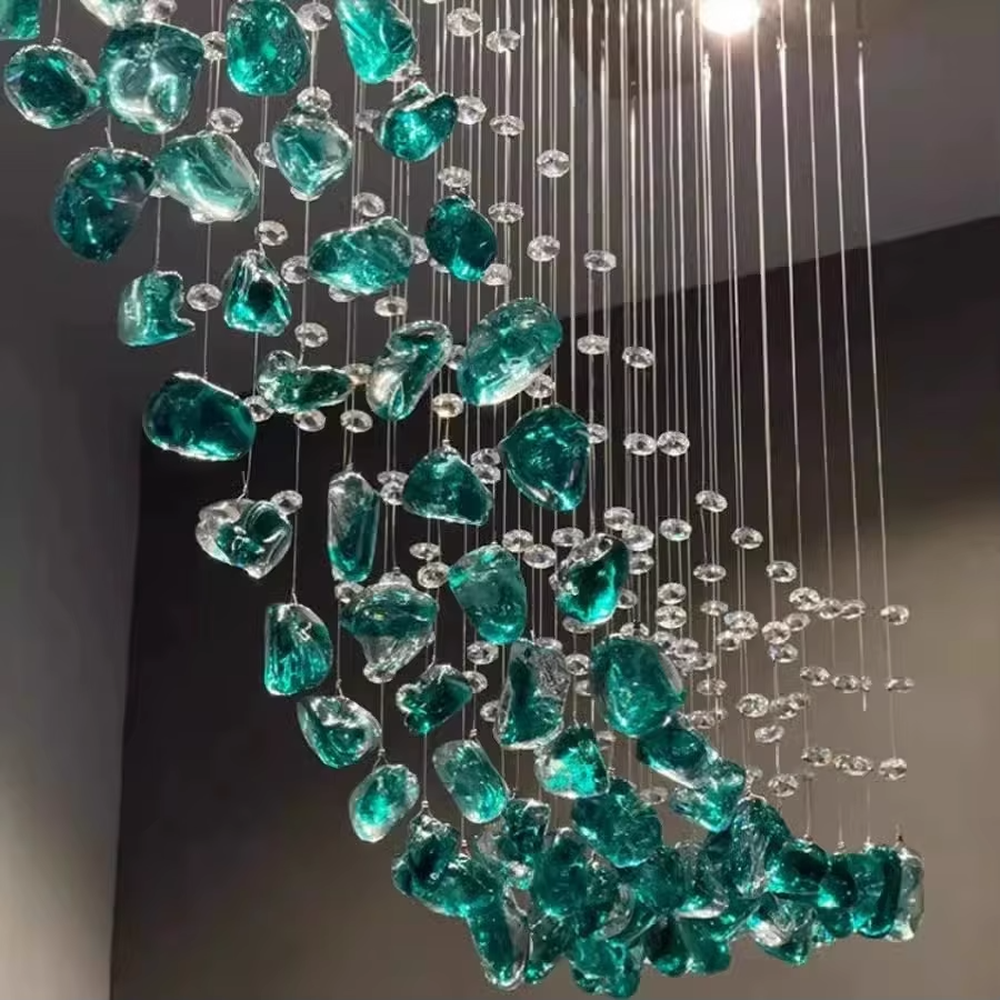 This is an artistic glass stone chandelier, with blue-green and transparent glass stones distributed irregularly in a hanging structure, featuring a modern artistic design with strong luxury artistic sense. It is used for space lighting and decoration, creating an artistic luxury atmosphere. It is suitable for modern luxury home living rooms, art exhibition halls, high-end restaurants and other places.