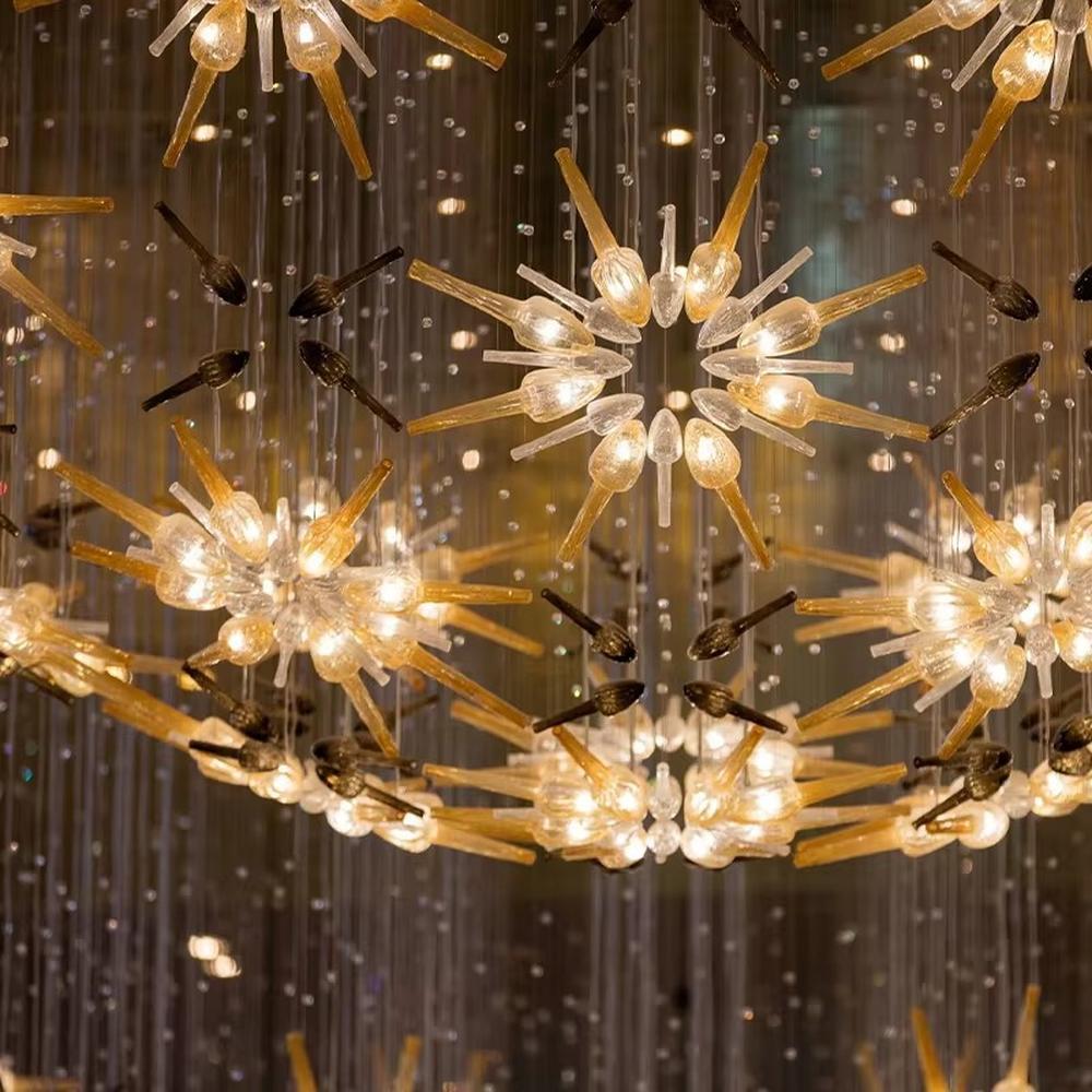 This is an artistic radial flower-shaped glass chandelier, with multi-layer colored glass components (gold, transparent, etc.) in a radial flower design, hanging structure, featuring strong artistic sense and visual hierarchy. It is used for space lighting and artistic decoration, creating a luxurious artistic atmosphere. It is suitable for high-end hotel lobbies, art exhibition halls, luxury clubs and other places.