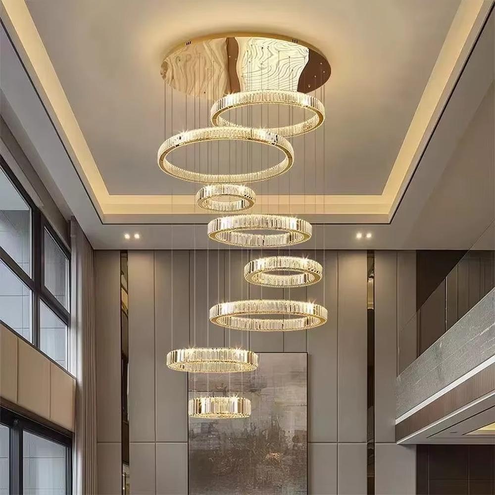 This is a luxury multi-layer circular crystal chandelier, with a golden base and staggered hanging crystal ring lamp bodies. It features a luxurious and grand design, shining brightly under light. It is used for space lighting and decoration, creating a high-end and luxurious ambiance. It is suitable for double-height living rooms in villas, lobbies of high-end hotels, luxury clubs and other places.