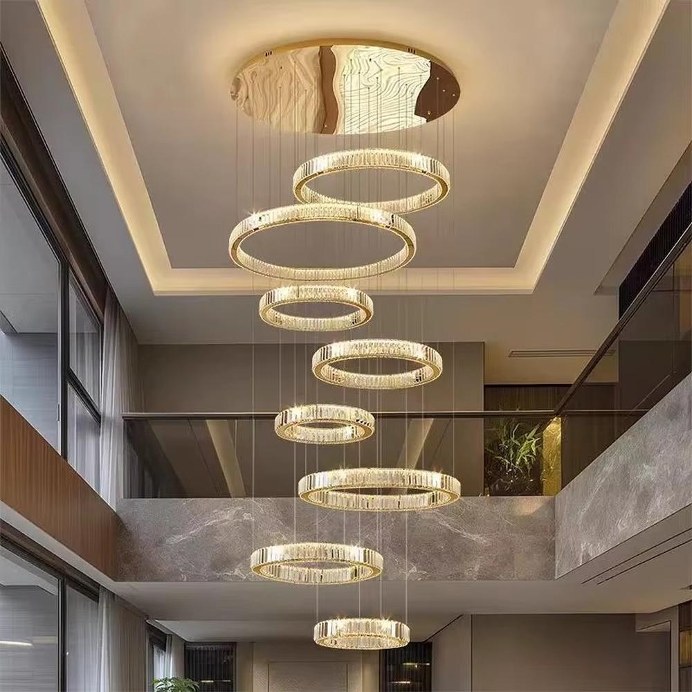 This is a luxury multi-layer circular crystal chandelier, with a golden base and staggered hanging crystal ring lamp bodies. It features a luxurious and grand design, shining brightly under light. It is used for space lighting and decoration, creating a high-end and luxurious ambiance. It is suitable for double-height living rooms in villas, lobbies of high-end hotels, luxury clubs and other places.