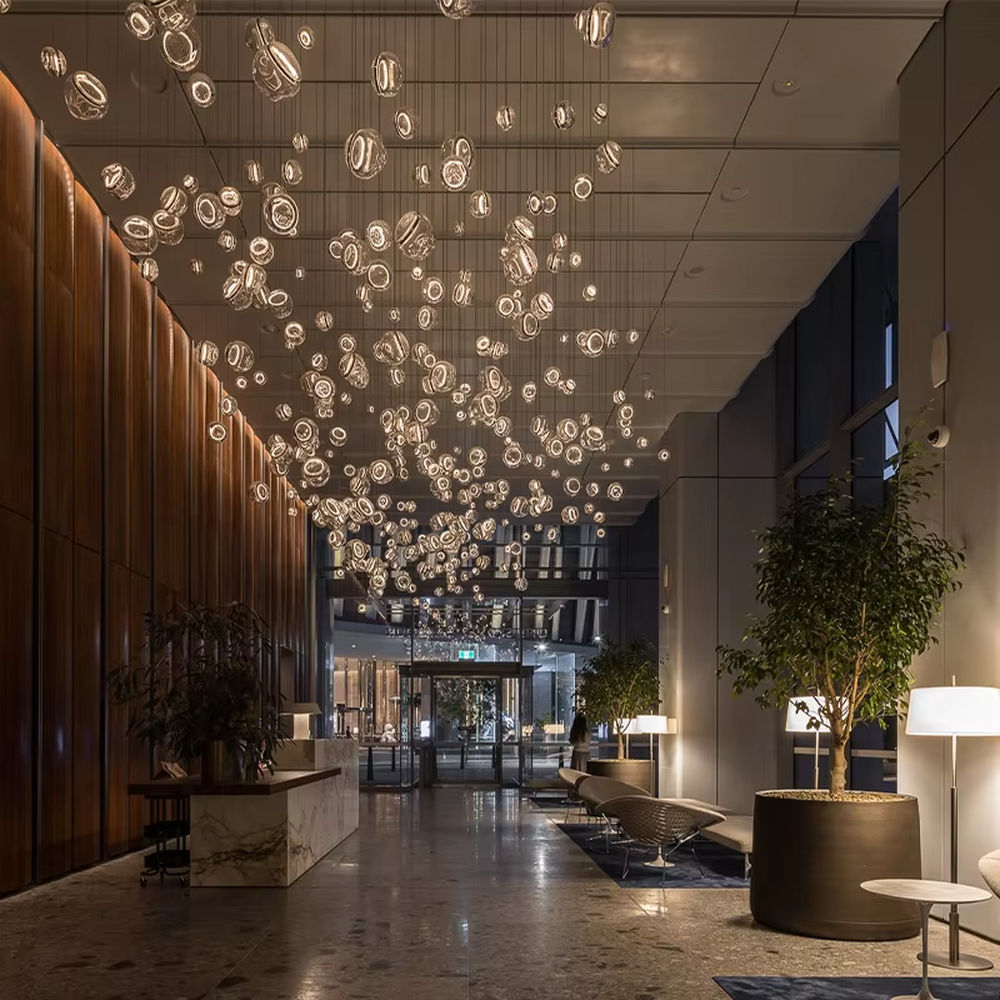 This is an artistic installation-style transparent glass ball chandelier, with numerous transparent glass balls of different sizes and shapes hanging in a scattered manner by thin wires. It features soft lighting and a strong sense of modern art and visual hierarchy. It is used for space lighting and artistic decoration, creating a modern artistic and ethereal atmosphere. Suitable for high-end hotel lobbies, art exhibition halls, atriums of large commercial centers and other places.
