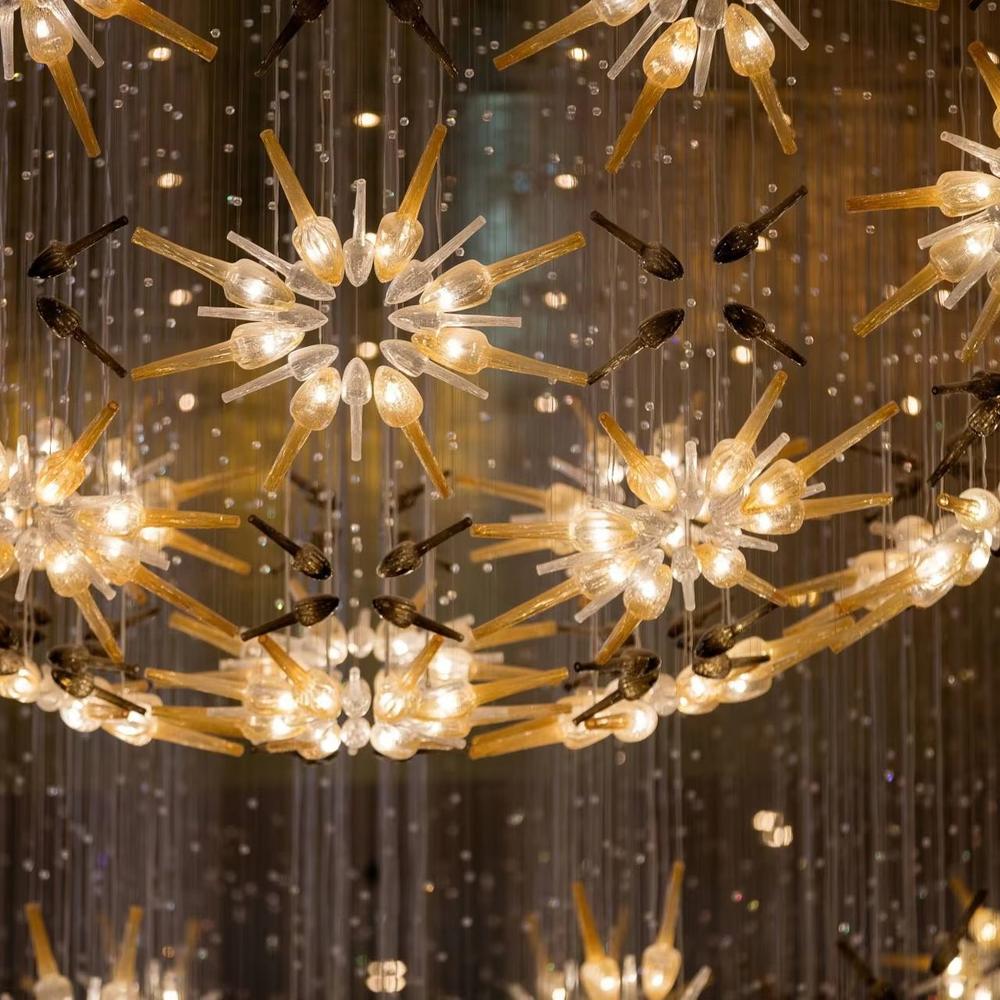 This is an artistic radial flower-shaped glass chandelier, with multi-layer colored glass components (gold, transparent, etc.) in a radial flower design, hanging structure, featuring strong artistic sense and visual hierarchy. It is used for space lighting and artistic decoration, creating a luxurious artistic atmosphere. It is suitable for high-end hotel lobbies, art exhibition halls, luxury clubs and other places.