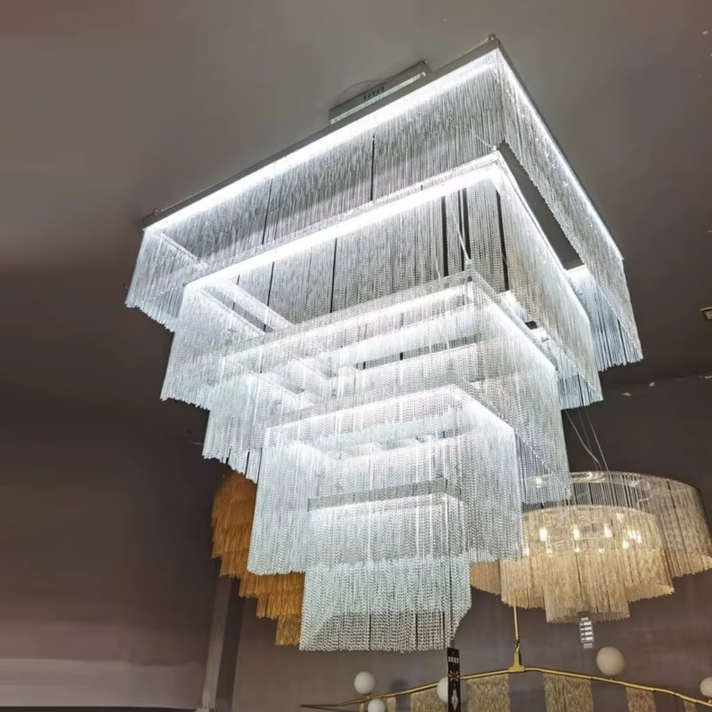 This is a modern artistic multi-layer square metal chain chandelier, composed of multi-layer square structures, paired with metal chains and LED light strips. It features soft and layered lighting, with a strong sense of modernity and spatial tension. It is used for space lighting and artistic decoration, creating a modern artistic and high-end atmosphere. Suitable for high-end hotel lobbies, art exhibition halls, high-ceiling spaces in luxury villas and other places.