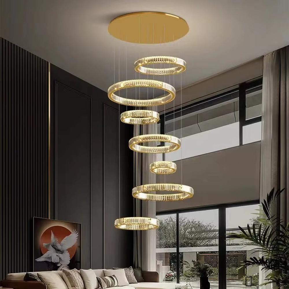 This is a luxury multi-layer circular crystal chandelier, with a golden base and staggered hanging crystal ring lamp bodies. It features a luxurious and grand design, shining brightly under light. It is used for space lighting and decoration, creating a high-end and luxurious ambiance. It is suitable for double-height living rooms in villas, lobbies of high-end hotels, luxury clubs and other places.