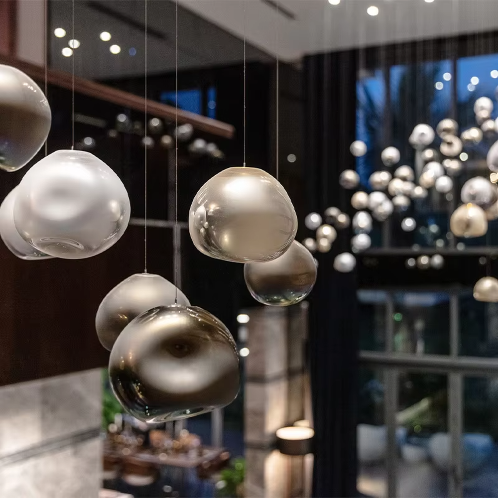 This is an artistic installation-style metal-textured glass sphere chandelier, with multiple irregular glass sphere lamps hanging in a scattered manner, featuring strong artistic sense, and the light reflects a unique visual effect. It is used for space lighting and artistic decoration, creating an artistic and modern atmosphere. Suitable for high-end hotel lobbies, art exhibition halls, modern art home living rooms and other places.