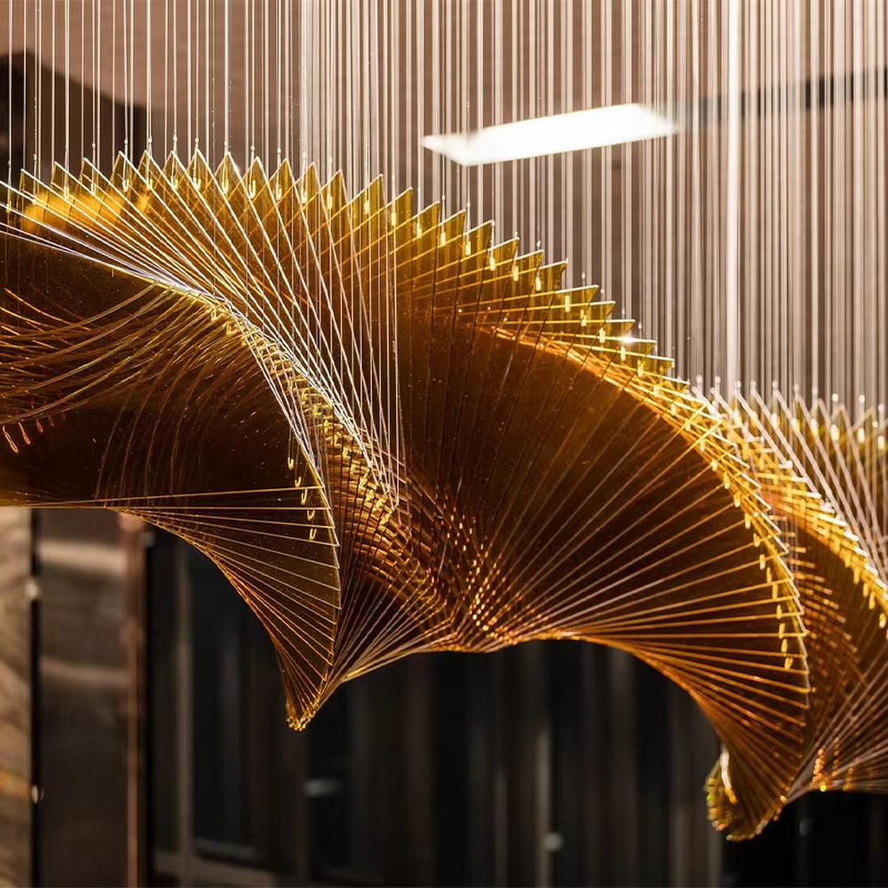 This is a modern artistic large wave-shaped metal art chandelier, with golden metal strips forming a three-dimensional wave shape, suspended by multiple thin wires. It features strong artistic tension and spatial decorativeness, with brilliant and grand lighting. It is used for space lighting and artistic installation decoration, creating a high-end artistic and luxurious atmosphere. Suitable for high-end hotel lobbies, luxury commercial clubs, art exhibition halls and other places.