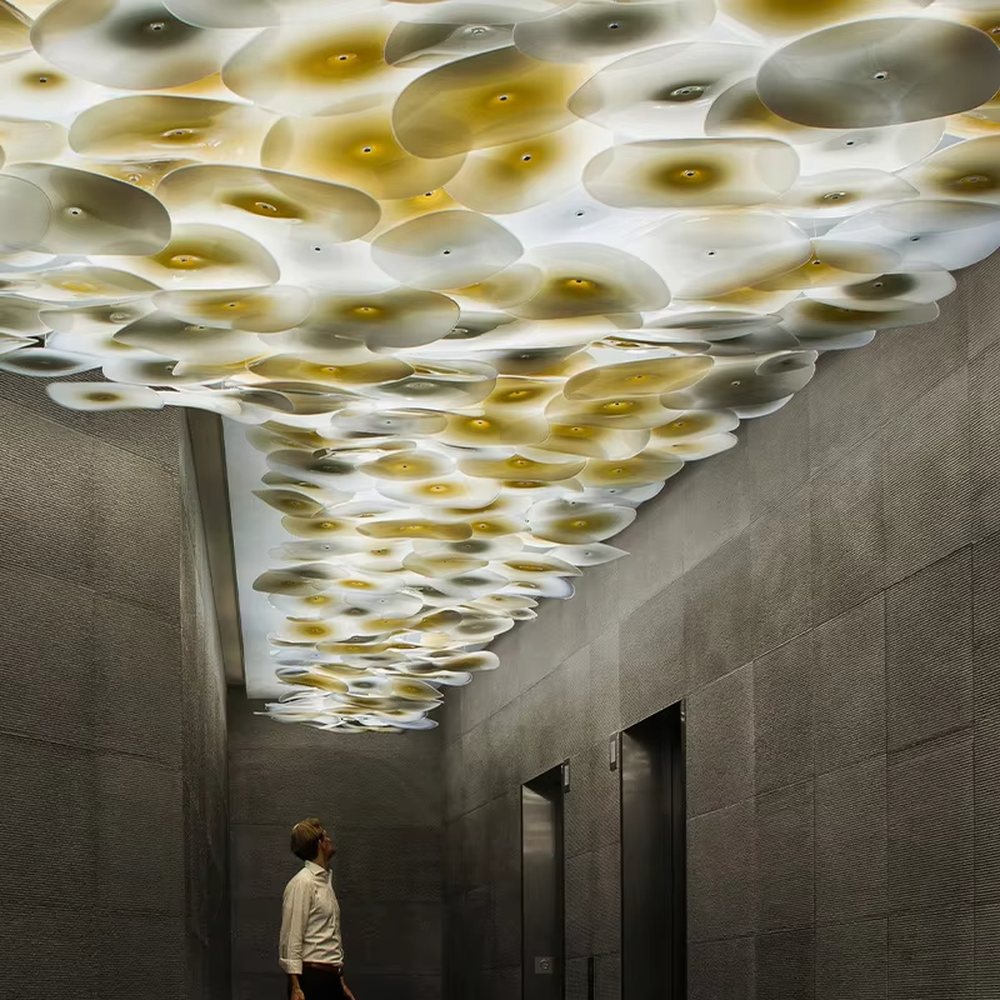 This is a modern artistic multi-layer disc glass art chandelier, composed of numerous gradient gold and white disc glass elements hanging in layers to form a three-dimensional ceiling decorative shape. It features soft and artistically layered lighting, with a strong sense of modern art and spatial decorativeness. It is used for space lighting and artistic installation decoration, creating a modern artistic and high-end elegant atmosphere. Suitable for high-end hotel lobby corridors, art exhibition halls, luxury commercial spaces and other places.