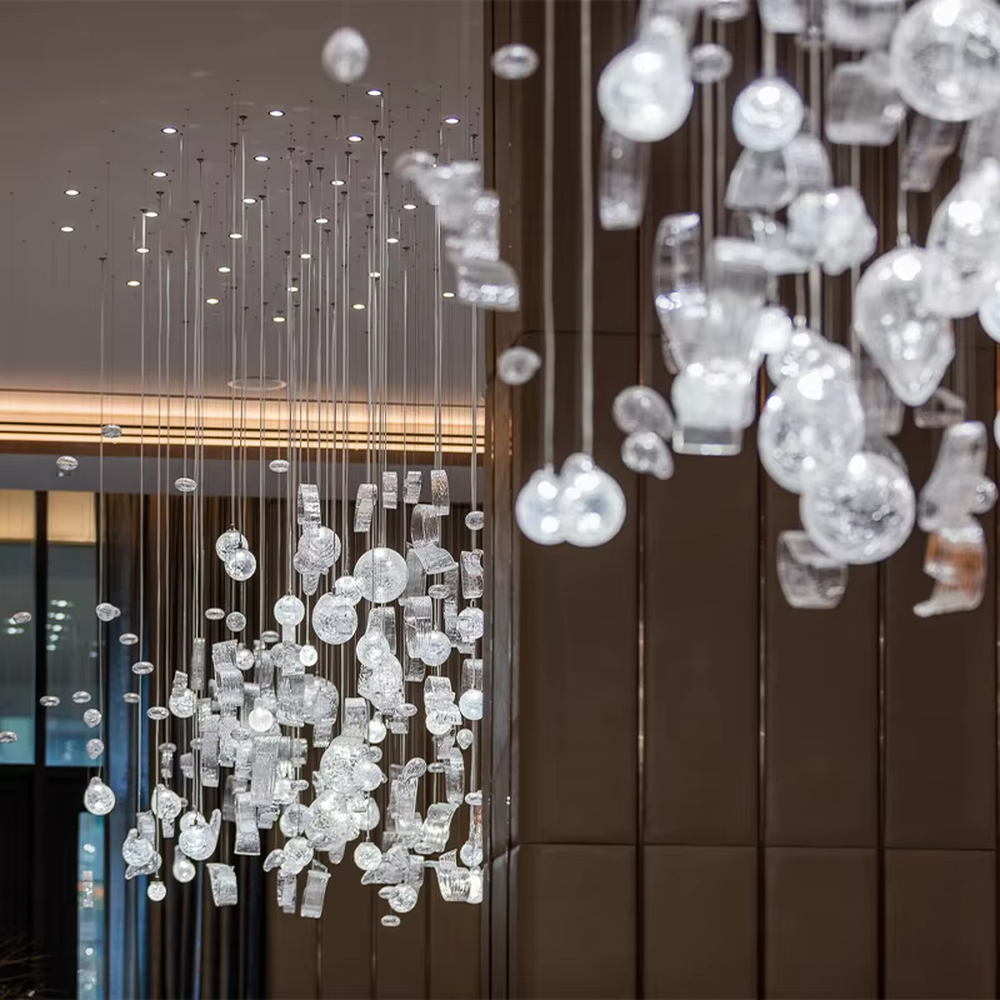 This is an artistic installation-style irregular transparent glass hanging chandelier, composed of numerous irregular transparent glass elements (spherical, block-shaped, etc.) hanging in a scattered manner by thin wires to form a three-dimensional layer. It features soft light refraction and a strong sense of modern art and spatial tension. It is used for space lighting and artistic decoration, creating a modern artistic and ethereal atmosphere. Suitable for high-end hotel lobbies, art exhibition halls, high-ceiling spaces in luxury villas and other places.