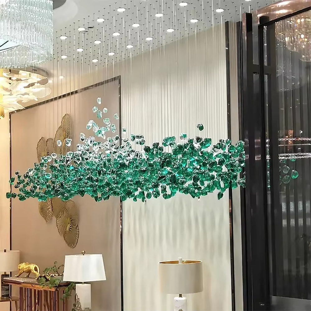This large-scale art crystal chandelier features a long, flowing shape made of green-white gradient crystal pieces, like suspended green plants or ocean waves. It serves both lighting and artistic decorative purposes, ideal for high-ceiling commercial spaces such as hotel lobbies, sales offices, and high-end clubs.