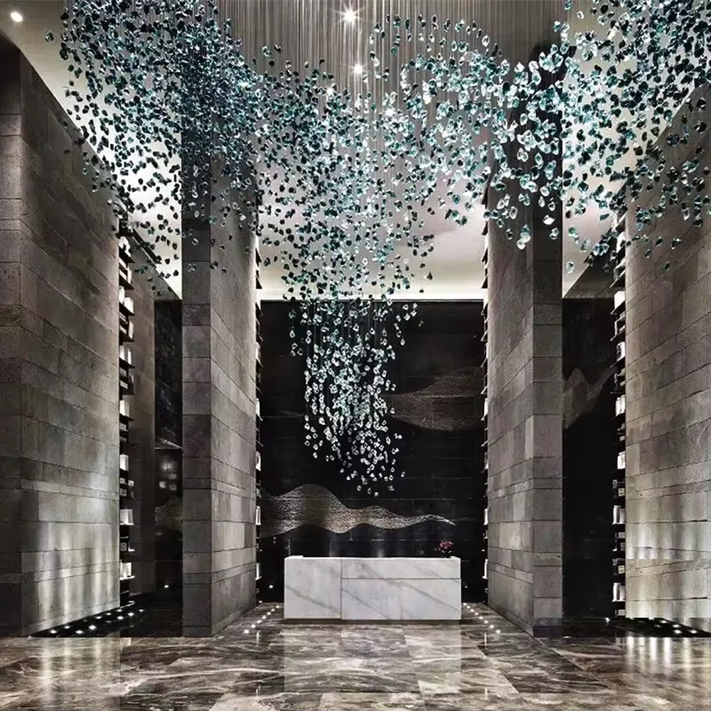 This large-scale art crystal chandelier features a long, flowing shape made of green-white gradient crystal pieces, like suspended green plants or ocean waves. It serves both lighting and artistic decorative purposes, ideal for high-ceiling commercial spaces such as hotel lobbies, sales offices, and high-end clubs.