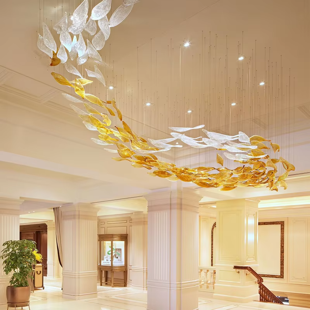 This large custom art glass chandelier features a streamlined school-of-fish/cloud-belt shape made of yellow-white gradient glass leaves, suspended in a floating manner, serving both lighting and artistic decoration purposes, ideal for high-ceiling commercial spaces such as sales offices, hotel lobbies, and high-end clubs.