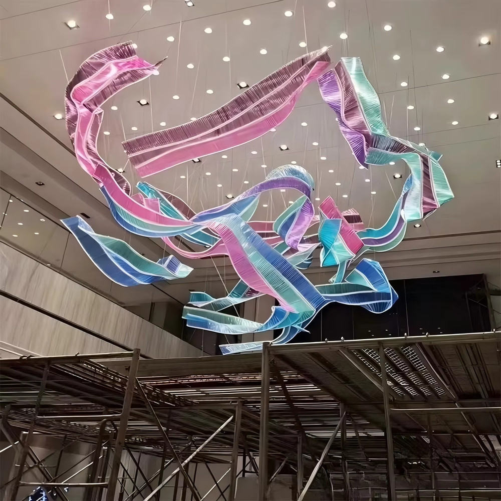 This large-scale art ribbon chandelier is made of semi-translucent material with pink-purple-blue-green gradients, featuring a flowing, pendant ribbon shape. It serves both lighting and artistic installation purposes, ideal for high-ceiling commercial spaces such as shopping mall atriums, hotel lobbies, and art galleries.