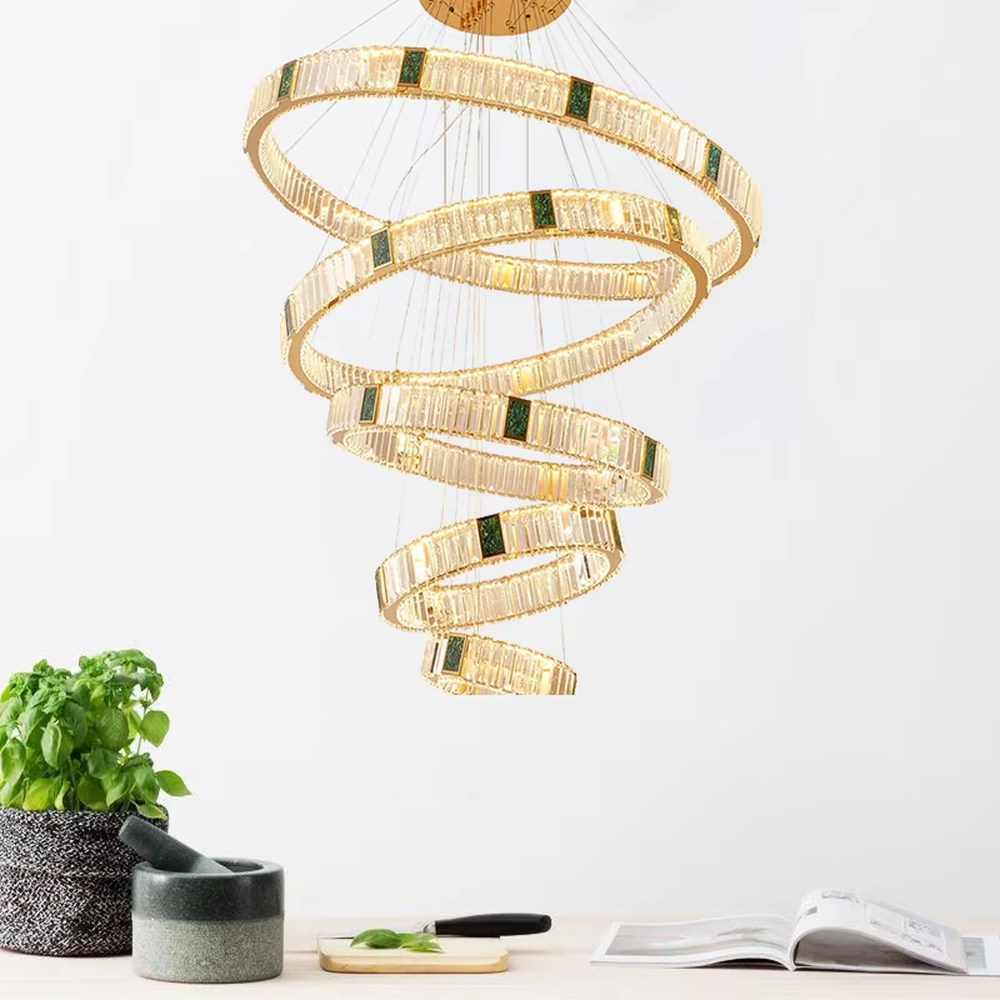 This is a light luxury artistic spiral crystal chandelier, featuring multi-layered circular crystal strips paired with a gold metal frame and emerald accents, shaped like a flowing tornado. Light refracts through the crystals to create brilliant and luxurious lighting effects, serving both lighting and artistic decoration purposes, suitable for high-ceiling spaces such as villa high-ceiling living rooms, duplex voids, hotel lobbies, and high-end clubs.