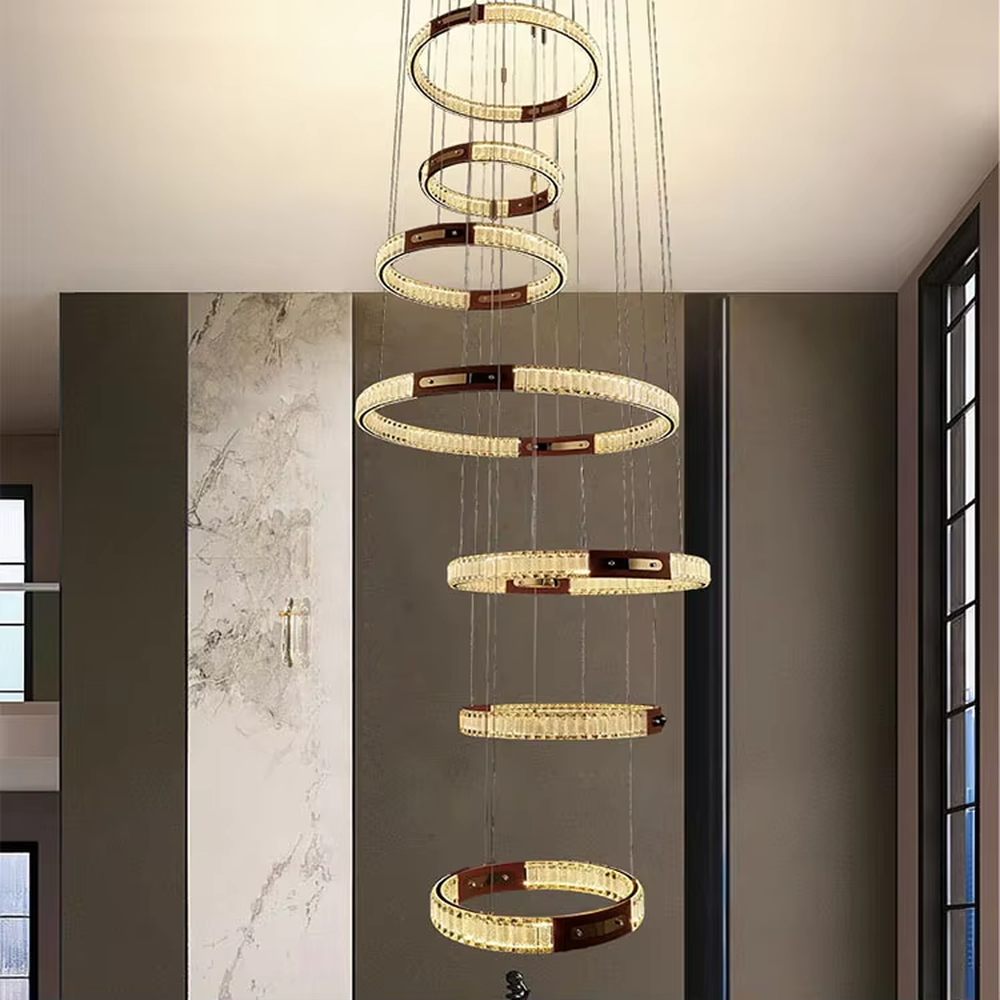 This is a light luxury style multi-layer staggered ring crystal chandelier, featuring a gold metal frame paired with transparent crystal strips. The layered ring shape resembles flowing light rhythm, emitting brilliant and luxurious light, serving both lighting and artistic decoration purposes, suitable for high-ceiling spaces such as villa high-ceiling living rooms, spiral staircases, hotel lobbies, and duplex voids.