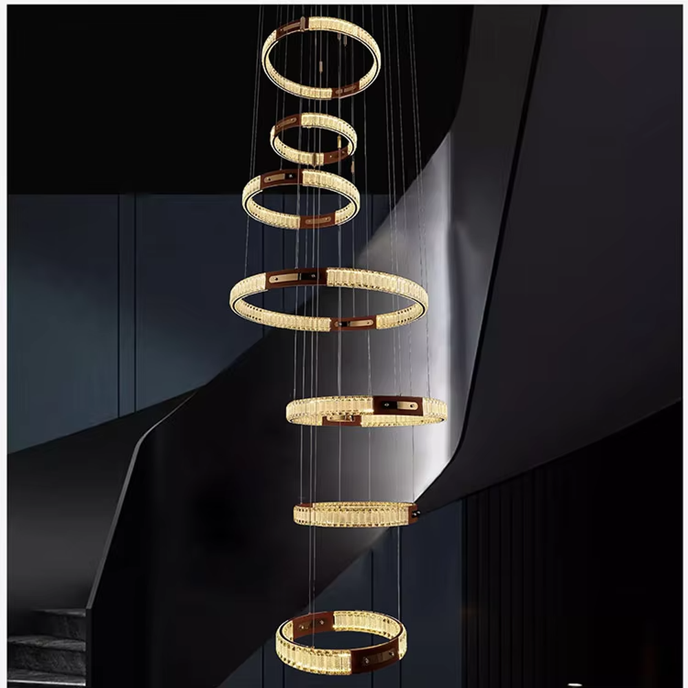 This is a light luxury style multi-layer staggered ring crystal chandelier, featuring a gold metal frame paired with transparent crystal strips. The layered ring shape resembles flowing light rhythm, emitting brilliant and luxurious light, serving both lighting and artistic decoration purposes, suitable for high-ceiling spaces such as villa high-ceiling living rooms, spiral staircases, hotel lobbies, and duplex voids.