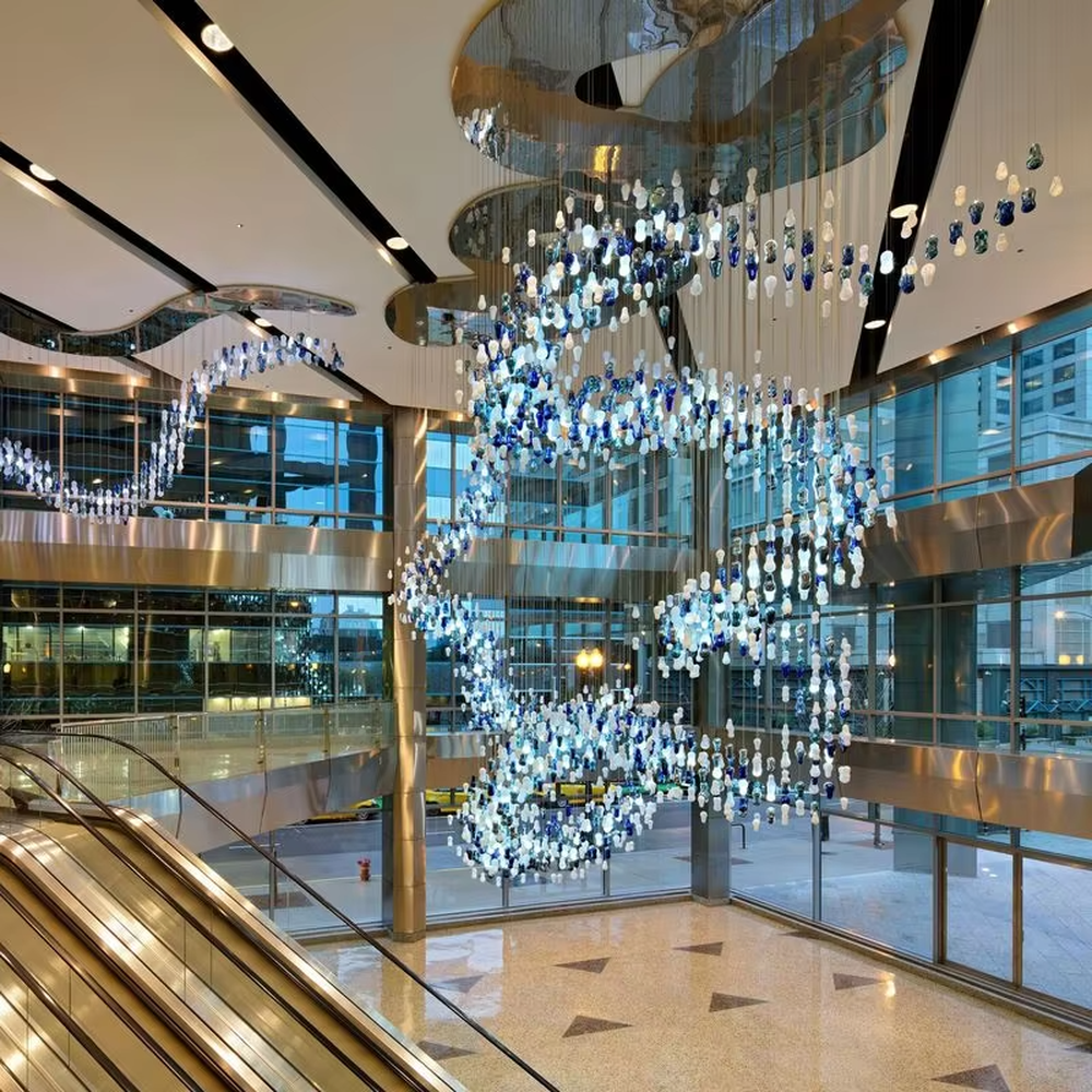 Art blue-white glass bead spiral chandelier (gradient color beads + curved shape), warm light effect, creating a dynamic artistic atmosphere for high-end public spaces.