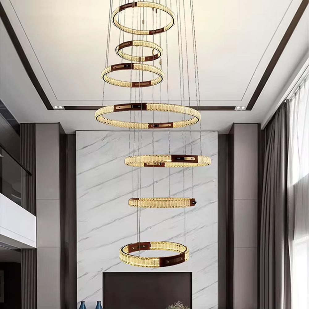 This is a light luxury style multi-layer staggered ring crystal chandelier, featuring a gold metal frame paired with transparent crystal strips. The layered ring shape resembles flowing light rhythm, emitting brilliant and luxurious light, serving both lighting and artistic decoration purposes, suitable for high-ceiling spaces such as villa high-ceiling living rooms, spiral staircases, hotel lobbies, and duplex voids.