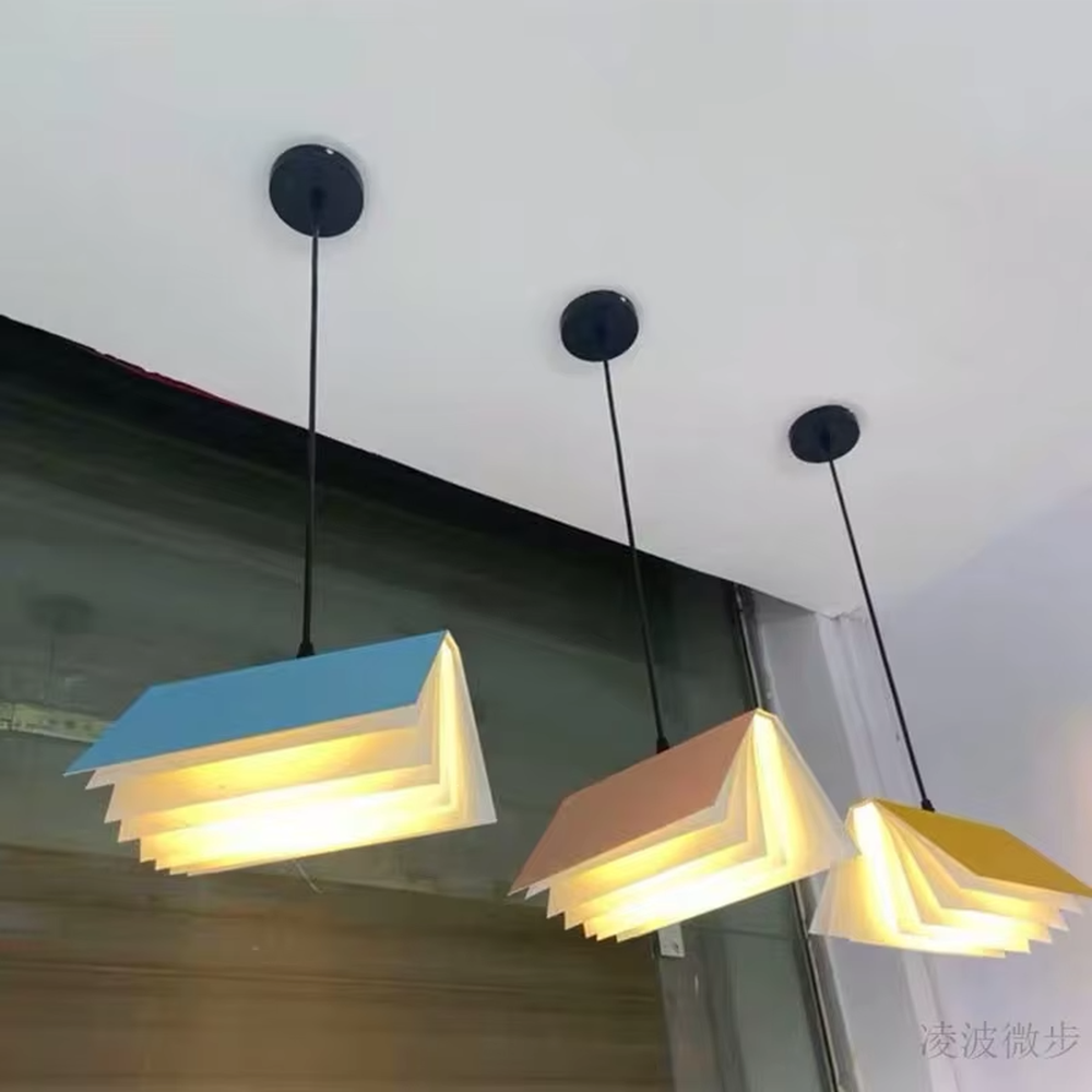 Creative origami book-shaped colorful hanging chandelier, folded structure + multi-color appearance (orange/pink/white/blue, etc.), soft and warm lighting, creating a literary creative atmosphere.