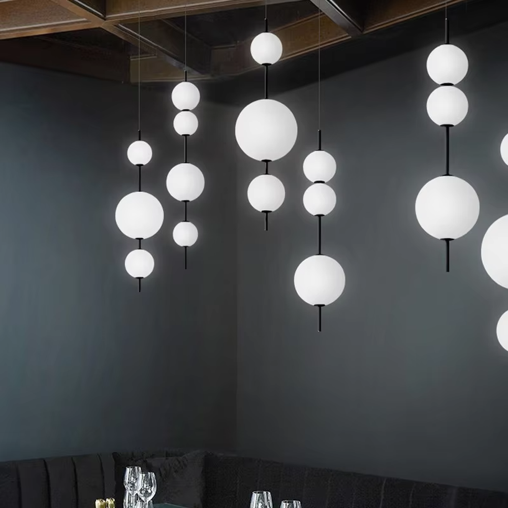 Modern tiered glass ball chandelier (black-white tiered balls + minimalist hanging rod), warm light effect, creating a simple and artistic space atmosphere.