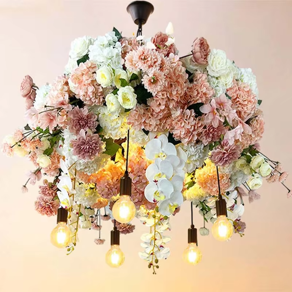 This is a romantic natural-style long strip floral chandelier, decorated with colorful artificial flowers (pink/purple/red roses) + green plants as the main body, paired with retro bulbs, featuring a fresh and romantic style, with warm and soft lighting.