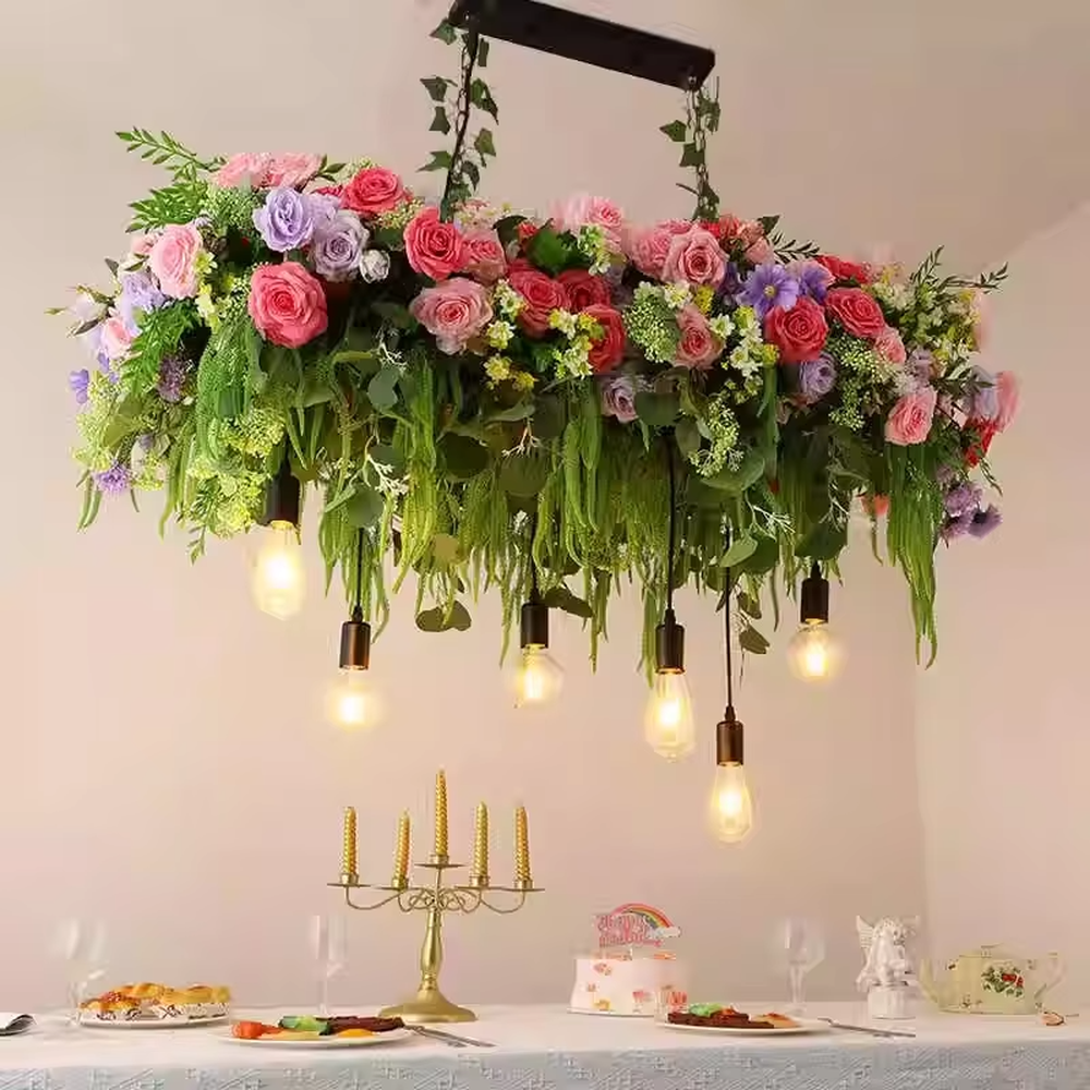 This is a romantic natural-style long strip floral chandelier, decorated with colorful artificial flowers (pink/purple/red roses) + green plants as the main body, paired with retro bulbs, featuring a fresh and romantic style, with warm and soft lighting.