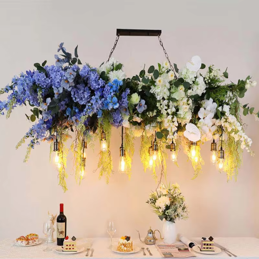 This is a natural and romantic floral retro chandelier, decorated with a large number of artificial flowers (pink and purple roses, etc.) and green plants (ferns, monstera leaves), paired with retro bulbs and a black metal frame. The design is natural and warm, with soft warm yellow lighting. It is used for space lighting and decoration, creating a natural romantic and warm retro atmosphere. Suitable for wedding venues, literary cafes, Nordic-style homestays, nature-themed restaurants and other places.