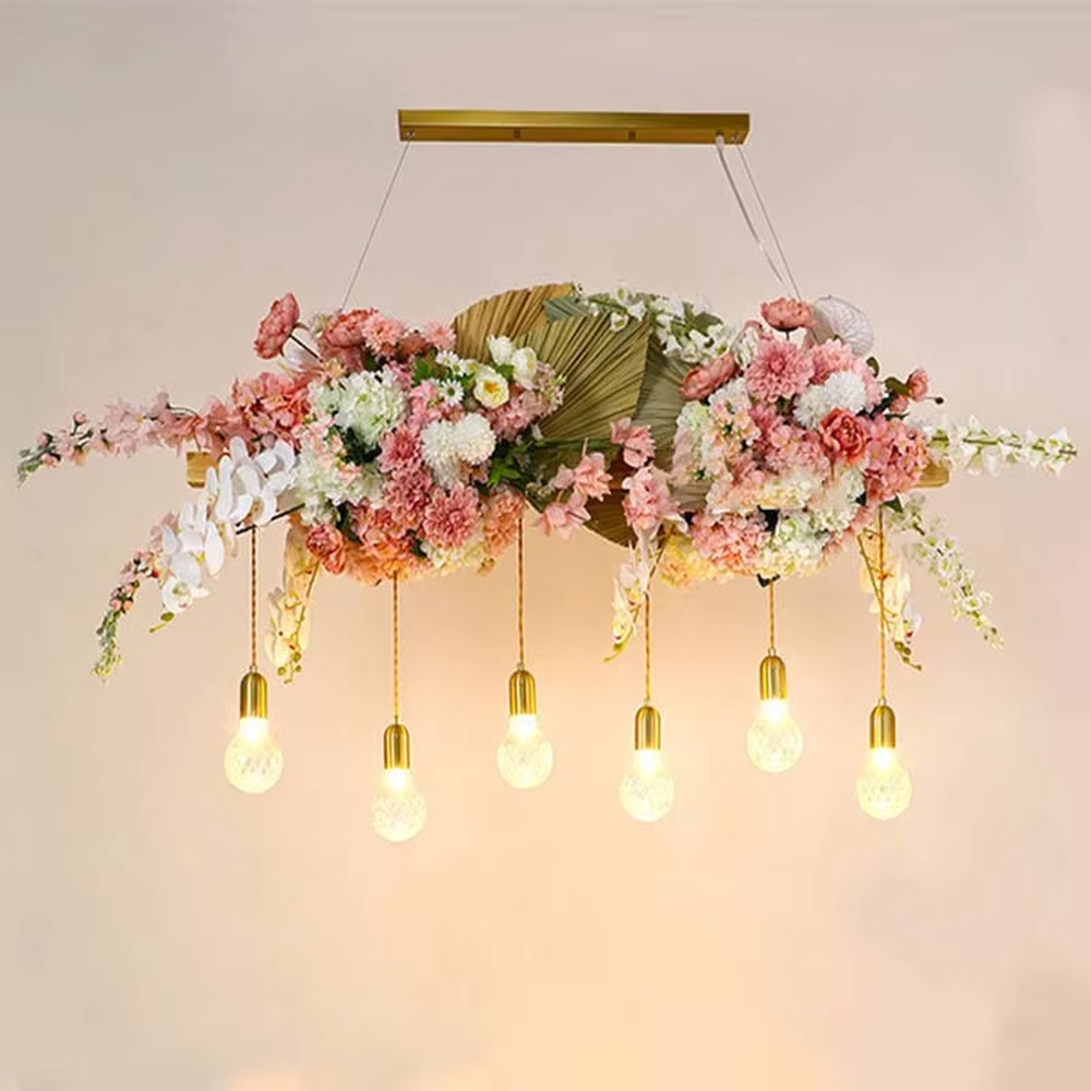 This is a romantic natural-style long strip floral chandelier, decorated with colorful artificial flowers (pink/purple/red roses) + green plants as the main body, paired with retro bulbs, featuring a fresh and romantic style, with warm and soft lighting.
