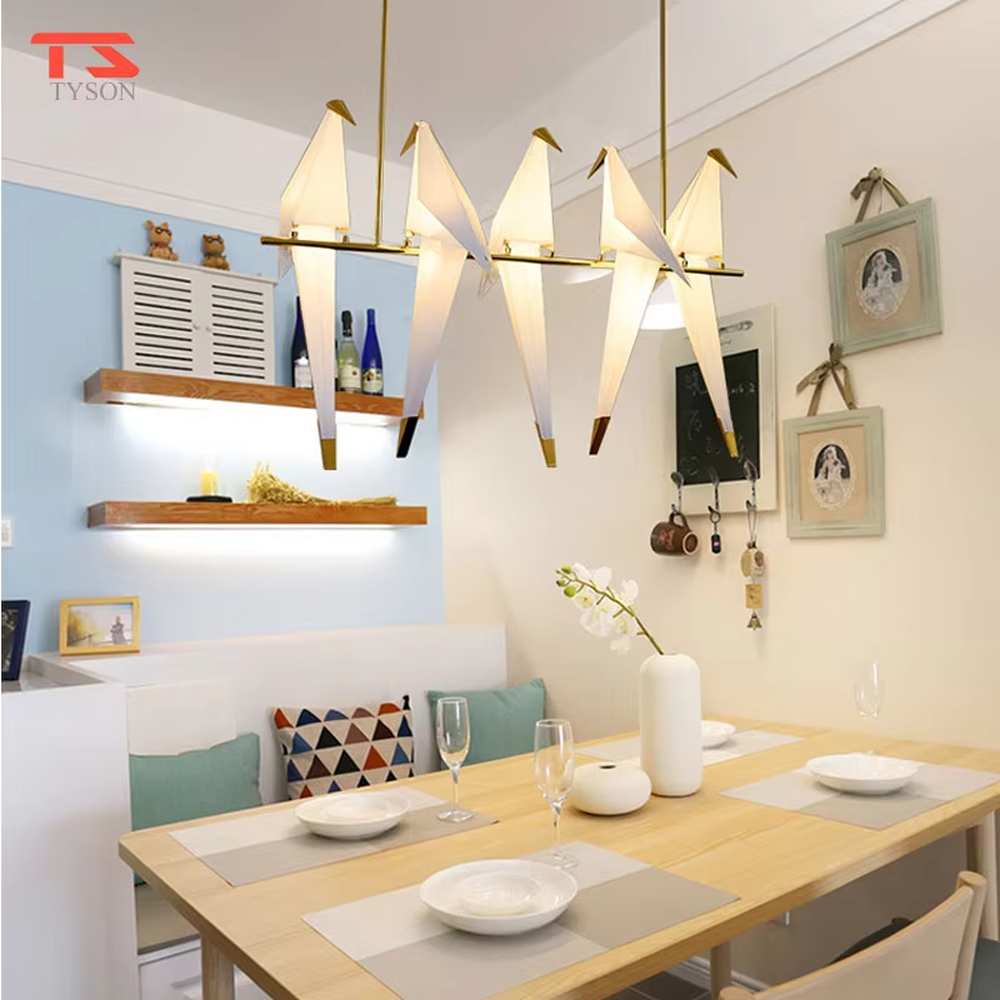 A modern art style linear chandelier in the shape of origami cranes, featuring a gold metal frame paired with translucent paper origami crane lampshades. It emits a soft and warm glow when lit, combining artistic decoration with lighting functionality, ideal for creating a soothing and romantic space atmosphere.
