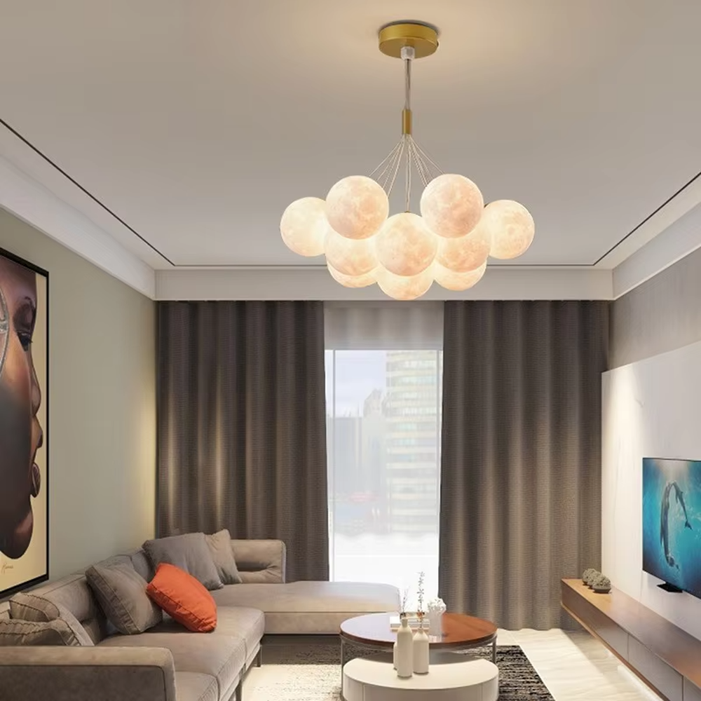 A modern light luxury style moon cluster chandelier, featuring a gold metal frame paired with multiple moon-textured glowing spheres and one colorful nebula sphere. It emits a soft and dreamy glow when lit, combining decorative appeal with practical illumination, ideal for creating a romantic and playful space atmosphere.