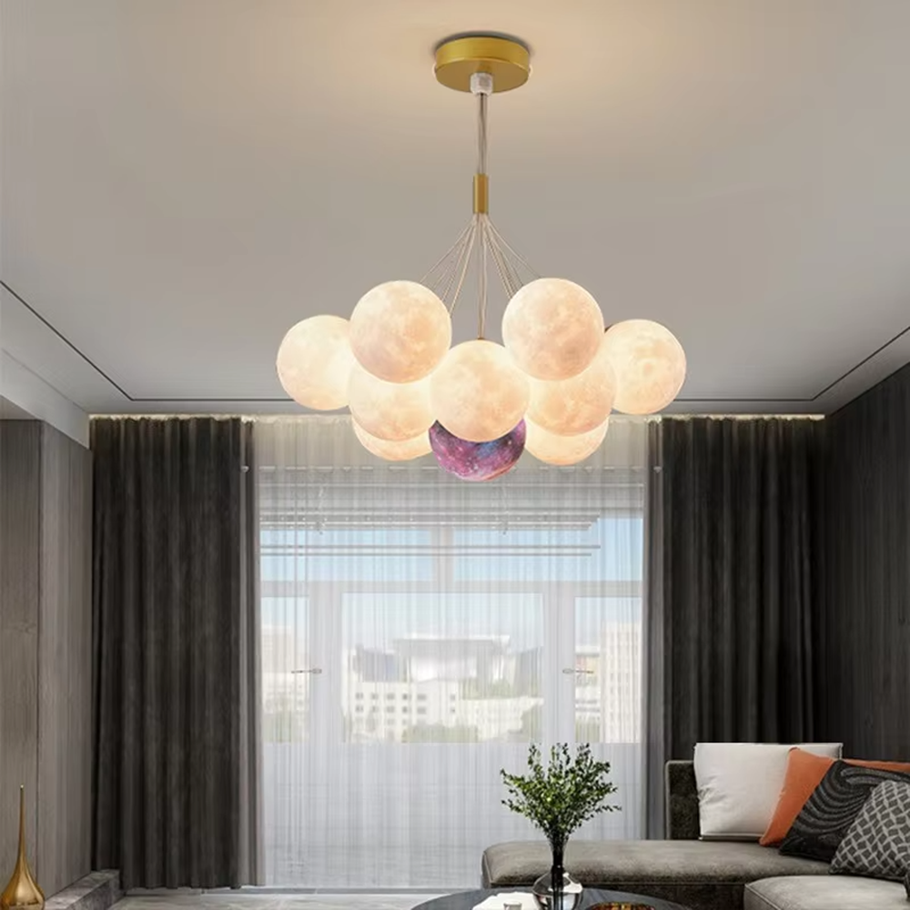 A modern light luxury style moon cluster chandelier, featuring a gold metal frame paired with multiple moon-textured glowing spheres and one colorful nebula sphere. It emits a soft and dreamy glow when lit, combining decorative appeal with practical illumination, ideal for creating a romantic and playful space atmosphere.