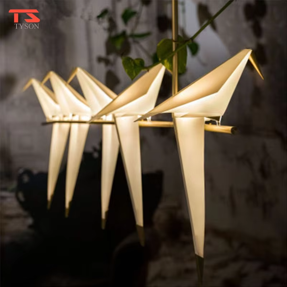 A modern art style linear chandelier in the shape of origami cranes, featuring a gold metal frame paired with translucent paper origami crane lampshades. It emits a soft and warm glow when lit, combining artistic decoration with lighting functionality, ideal for creating a soothing and romantic space atmosphere.
