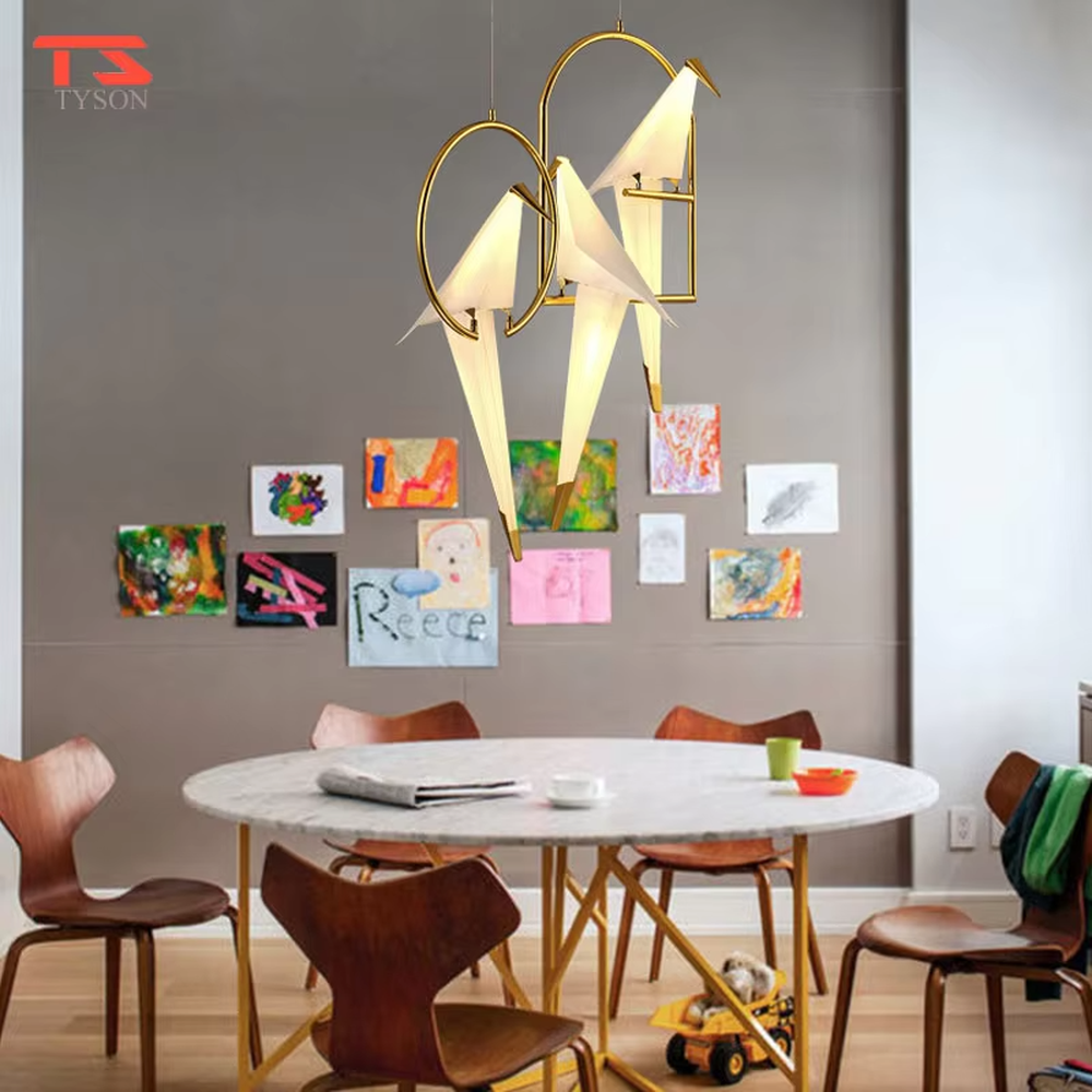 A modern art light luxury style origami crane chandelier, featuring a gold metal ring frame paired with an origami-style white translucent lampshade, shaped like an origami crane perched in a gold ring. It emits a soft and warm glow when lit, combining decorative appeal with practical illumination, ideal for creating an elegant and soothing space atmosphere.