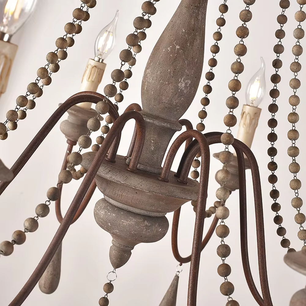 A French country retro style 6-head chandelier, featuring a weathered solid wood main frame paired with iron lamp arms, wooden bead chains and teardrop pendants, using candle-shaped bulbs. It emits a warm and soft glow when lit, combining decorative appeal with practical illumination, ideal for creating a cozy and retro space atmosphere.