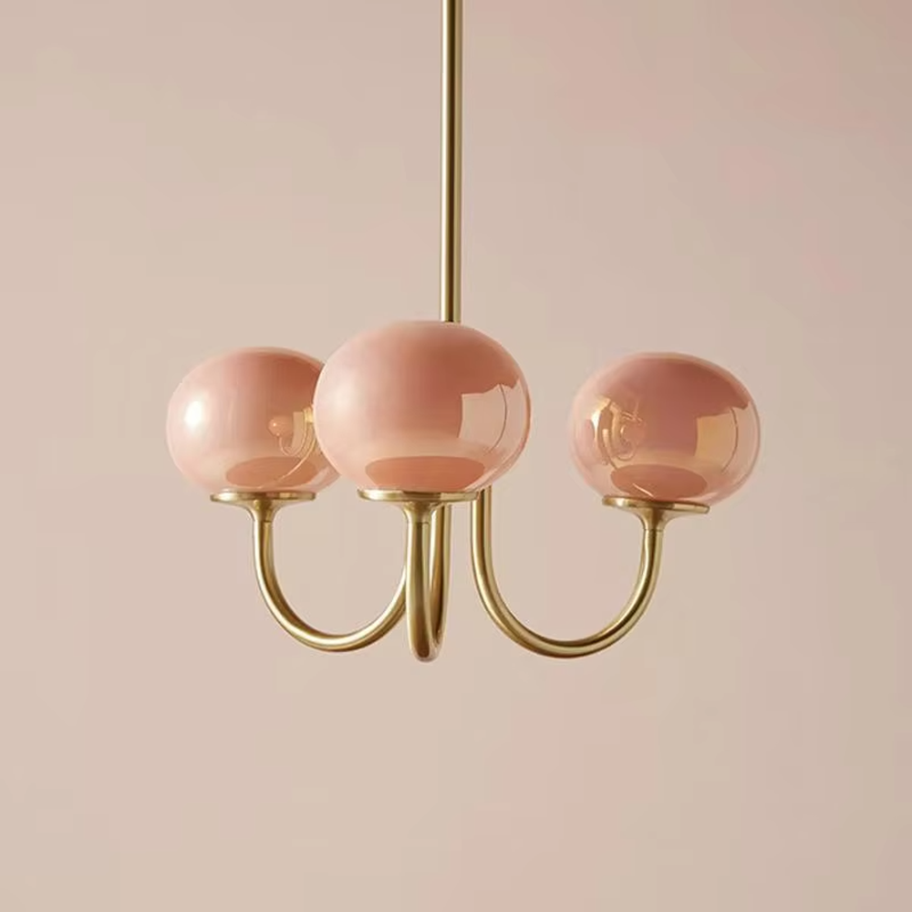 A French girly-style 3-head chandelier, featuring a gold metal curved frame paired with pink gradient glass ball lampshades (larger in the center, smaller on both sides). It emits a soft warm glow when lit, combining decorative appeal with practical illumination, ideal for creating a sweet and romantic space atmosphere.