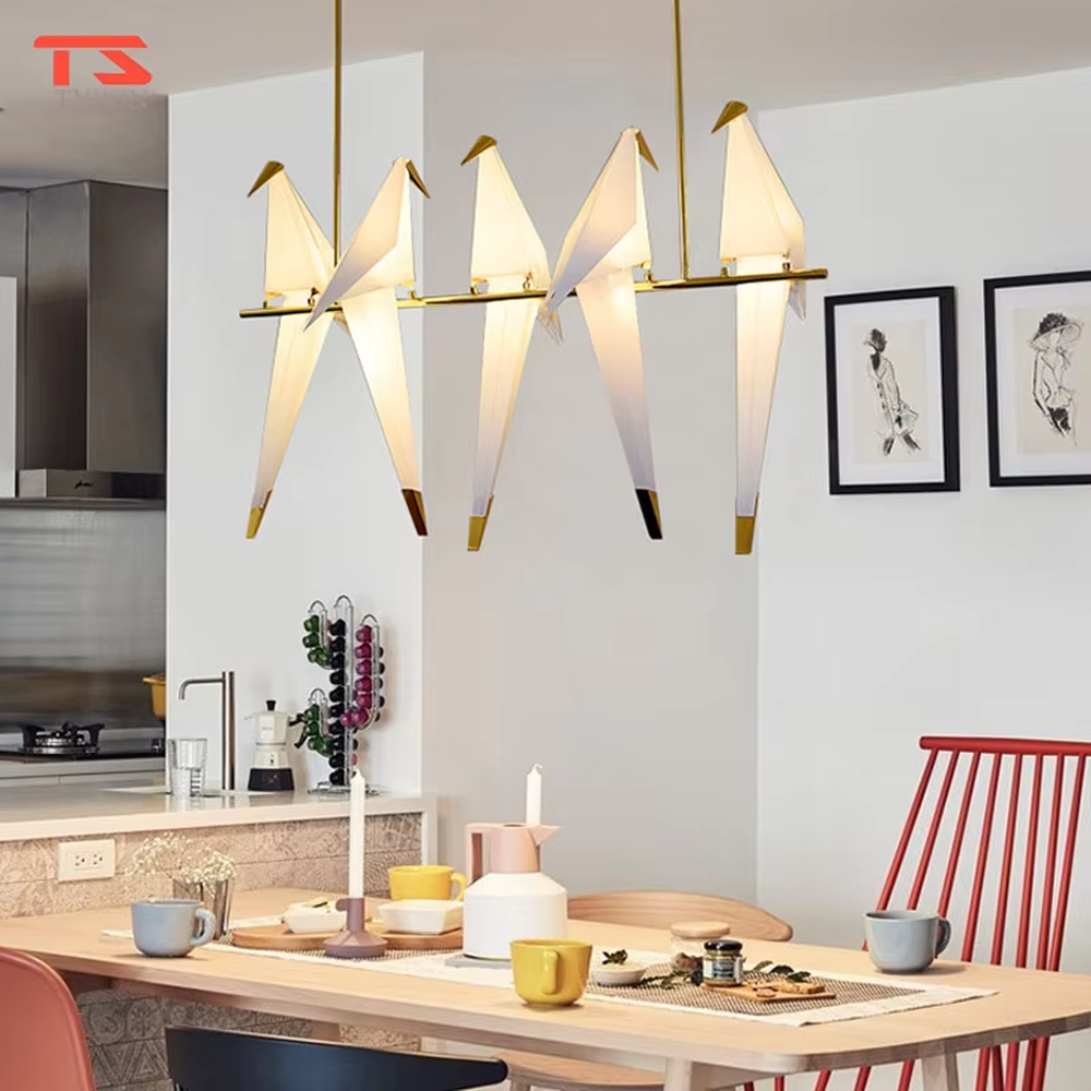 A modern art style linear chandelier in the shape of origami cranes, featuring a gold metal frame paired with translucent paper origami crane lampshades. It emits a soft and warm glow when lit, combining artistic decoration with lighting functionality, ideal for creating a soothing and romantic space atmosphere.

