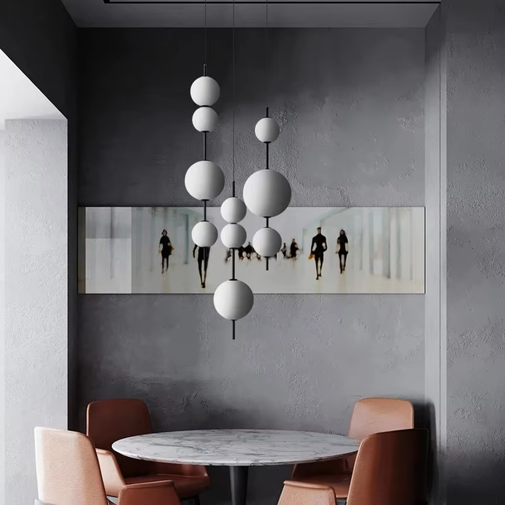 This minimalist string ball chandelier features black suspension rods connecting white spherical lampshades of varying sizes, with light refracting a soft halo through the frosted shades, serving both lighting and decorative purposes, suitable for modern minimalist commercial spaces such as restaurants and cafes.