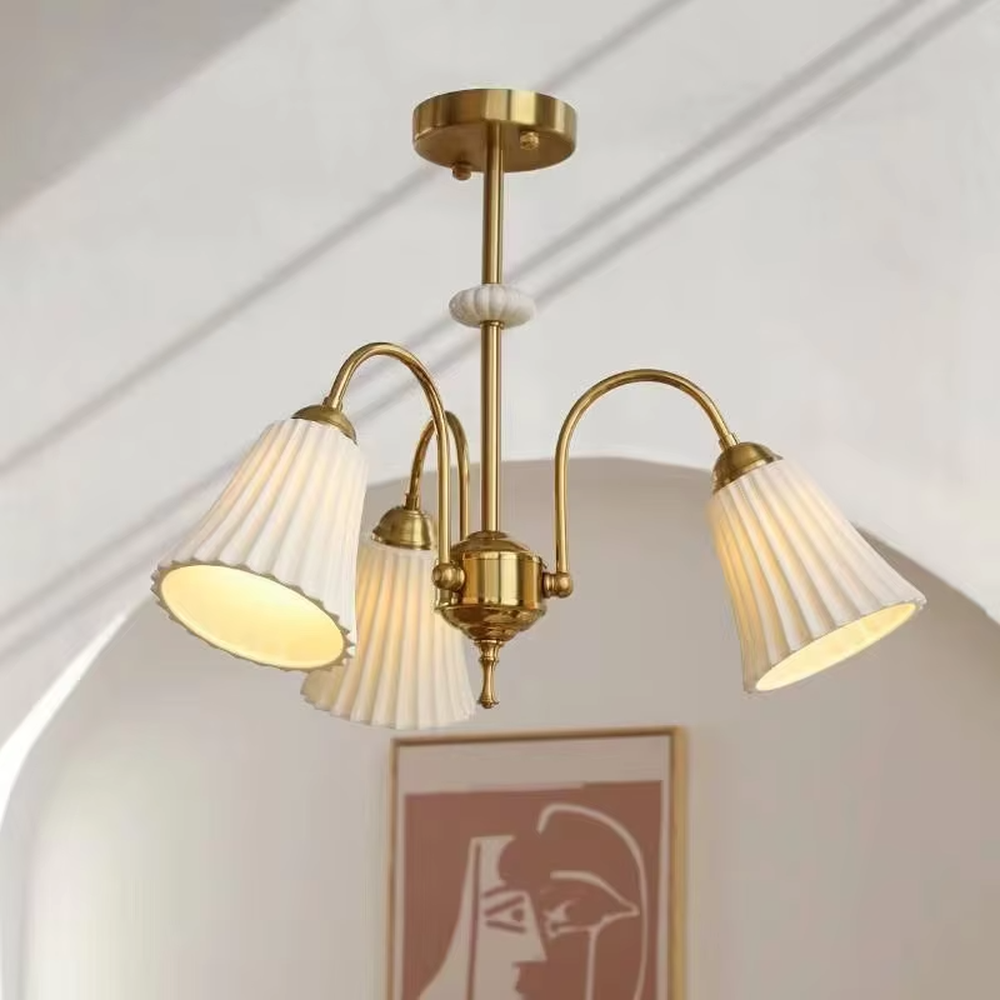 A French retro light luxury style 3-head chandelier, featuring a brass-colored metal frame paired with pleated fabric lampshades. It emits a soft and warm glow when lit, combining decorative appeal with practical illumination, ideal for creating an elegant and romantic space atmosphere.