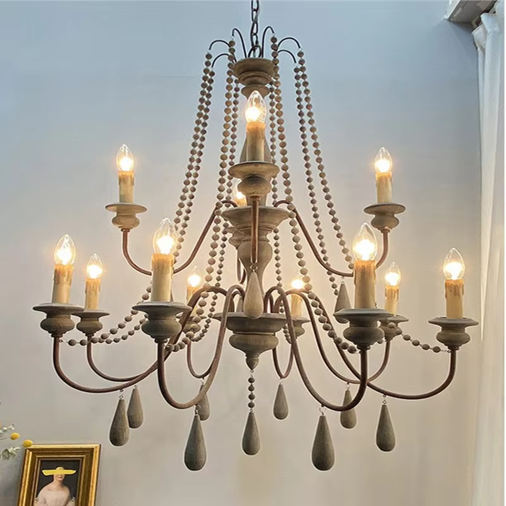 A French country retro style 6-head chandelier, featuring a weathered solid wood main frame paired with iron lamp arms, wooden bead chains and teardrop pendants, using candle-shaped bulbs. It emits a warm and soft glow when lit, combining decorative appeal with practical illumination, ideal for creating a cozy and retro space atmosphere.