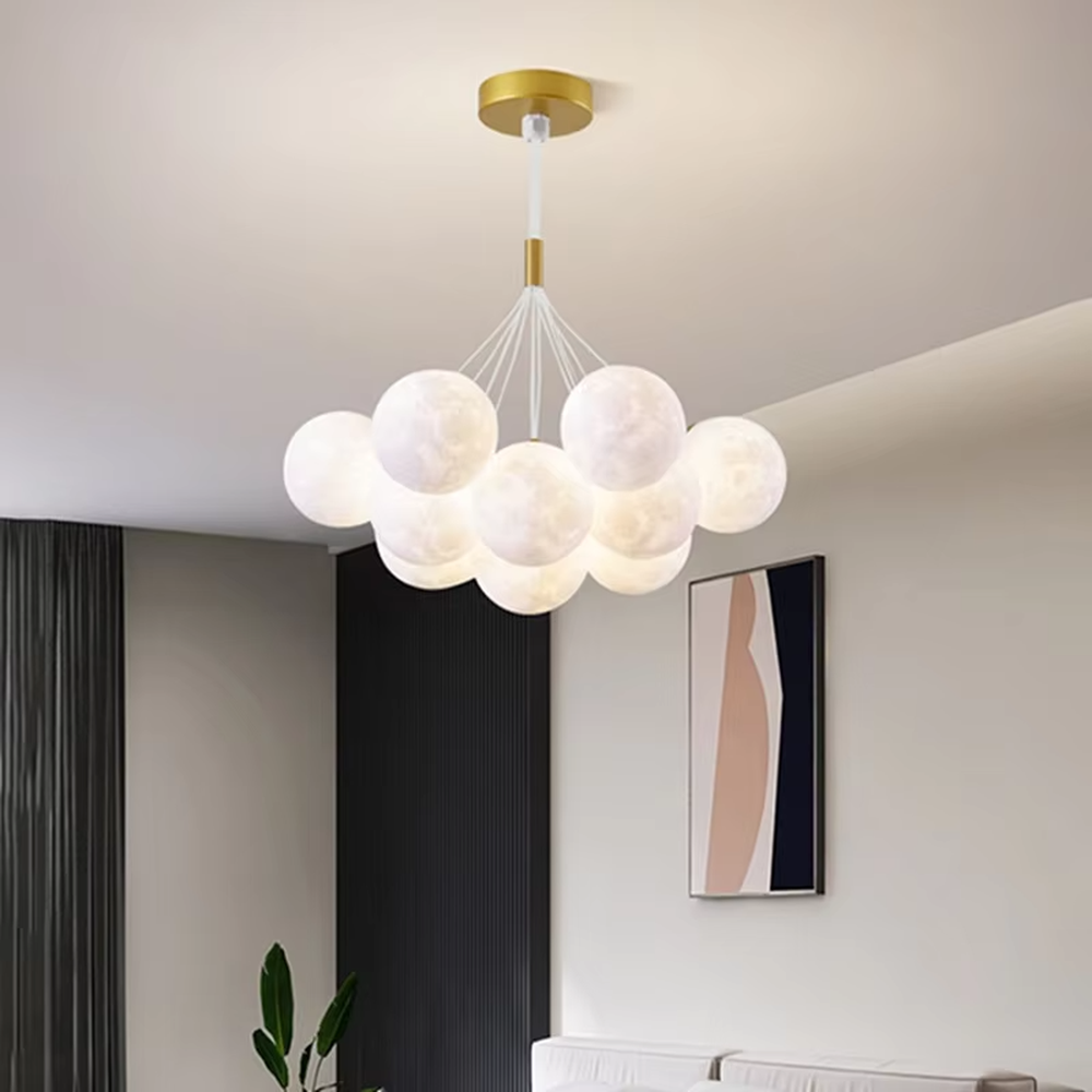 A modern light luxury style moon cluster chandelier, featuring a gold metal frame paired with multiple moon-textured glowing spheres and one colorful nebula sphere. It emits a soft and dreamy glow when lit, combining decorative appeal with practical illumination, ideal for creating a romantic and playful space atmosphere.