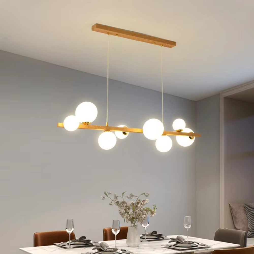 Nordic-style gold linear chandelier with a wood-like finish, paired with multiple round milk-white glass ball lampshades. It features a simple and lightweight design, emitting soft and gentle light, serving as a modern home lighting fixture that combines illumination and decoration.

