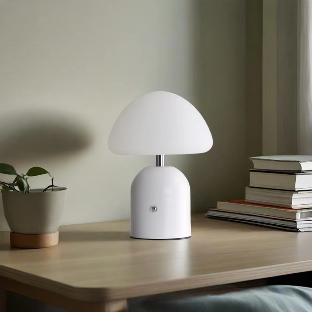 This is a minimalist mushroom-shaped table lamp with a white rounded mushroom lampshade and a simple base, featuring a fresh and cute design with a warm ambiance. It is used for local desktop lighting and decoration, creating a minimalist and warm atmosphere. It is suitable for Nordic-style home bedrooms, children's rooms, minimalist office spaces and other places.