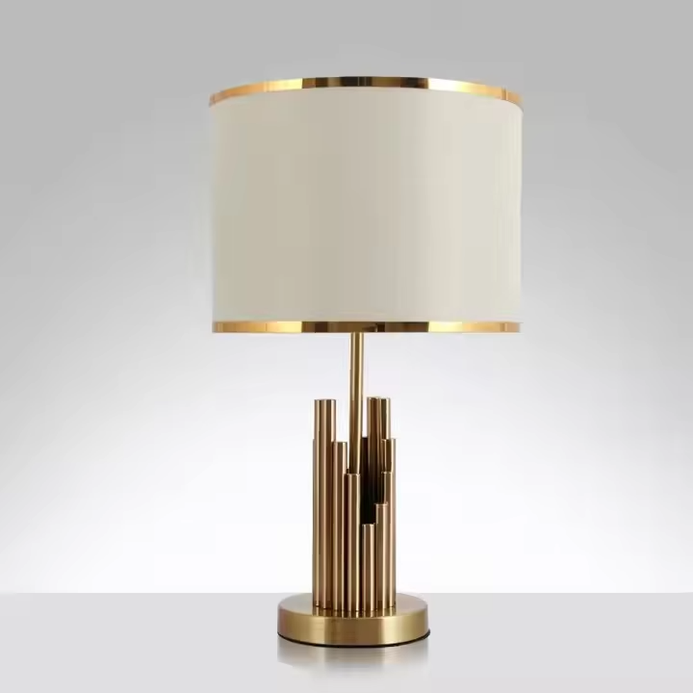 This is a modern luxury-style table lamp with a golden metal multi-column base and a beige fabric lampshade, featuring a simple and elegant design. It is used for local desktop lighting and decoration, combining practicality and aesthetics. It is suitable for modern home bedroom bedside tables, living room side tables, high-end hotel guest rooms, luxury apartment living spaces and other places.