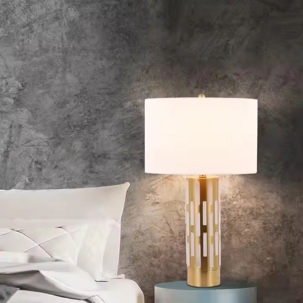 This is a modern minimalist table lamp with a golden base decorated with white vertical strips and a white fabric lampshade, featuring a simple and elegant design. It is used for local desktop lighting and decoration, combining practicality and aesthetics. It is suitable for modern home bedroom bedside tables, living room side tables, high-end hotel guest rooms, luxury apartment living spaces and other places.
