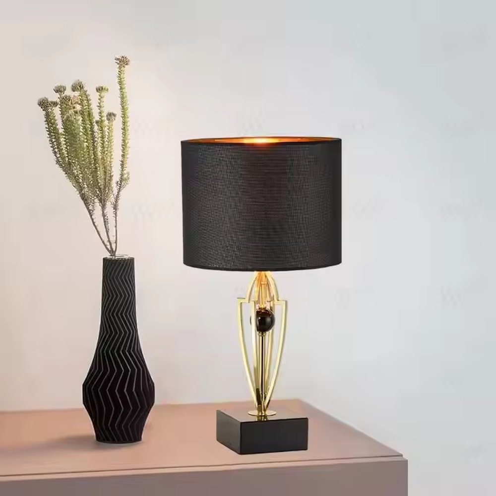 This is a luxurious retro-style table lamp with a golden metal bracket, a black square base, and a black fabric lampshade. It features a grand and elegant design with artistic texture. It is used for local desktop lighting and decoration, creating a luxurious retro ambiance. It is suitable for luxury-style home bedrooms, high-end hotel guest rooms, art exhibition halls and other places.