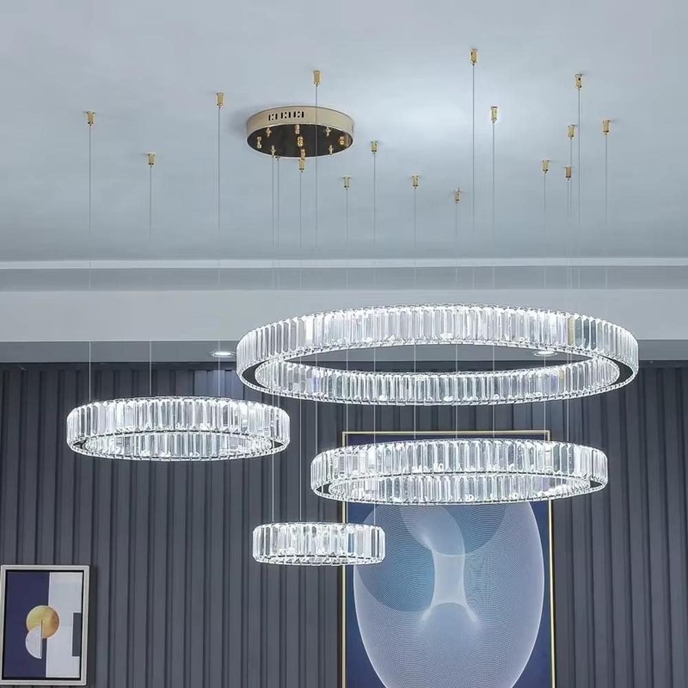 This modern light luxury multi-ring crystal chandelier consists of multiple crystal rings of varying sizes suspended in a staggered layout, each inlaid with transparent long crystals and adjustable via gold suspension wires. When lit, light refracts through the crystal to emit a brilliant and soft glow, combining layered design with an ambient atmosphere. Ideal for high-ceiling living rooms, villa foyers, hotel lobbies, or duplex spaces, it adds an exquisite and sophisticated touch to modern light luxury or minimalist environments.